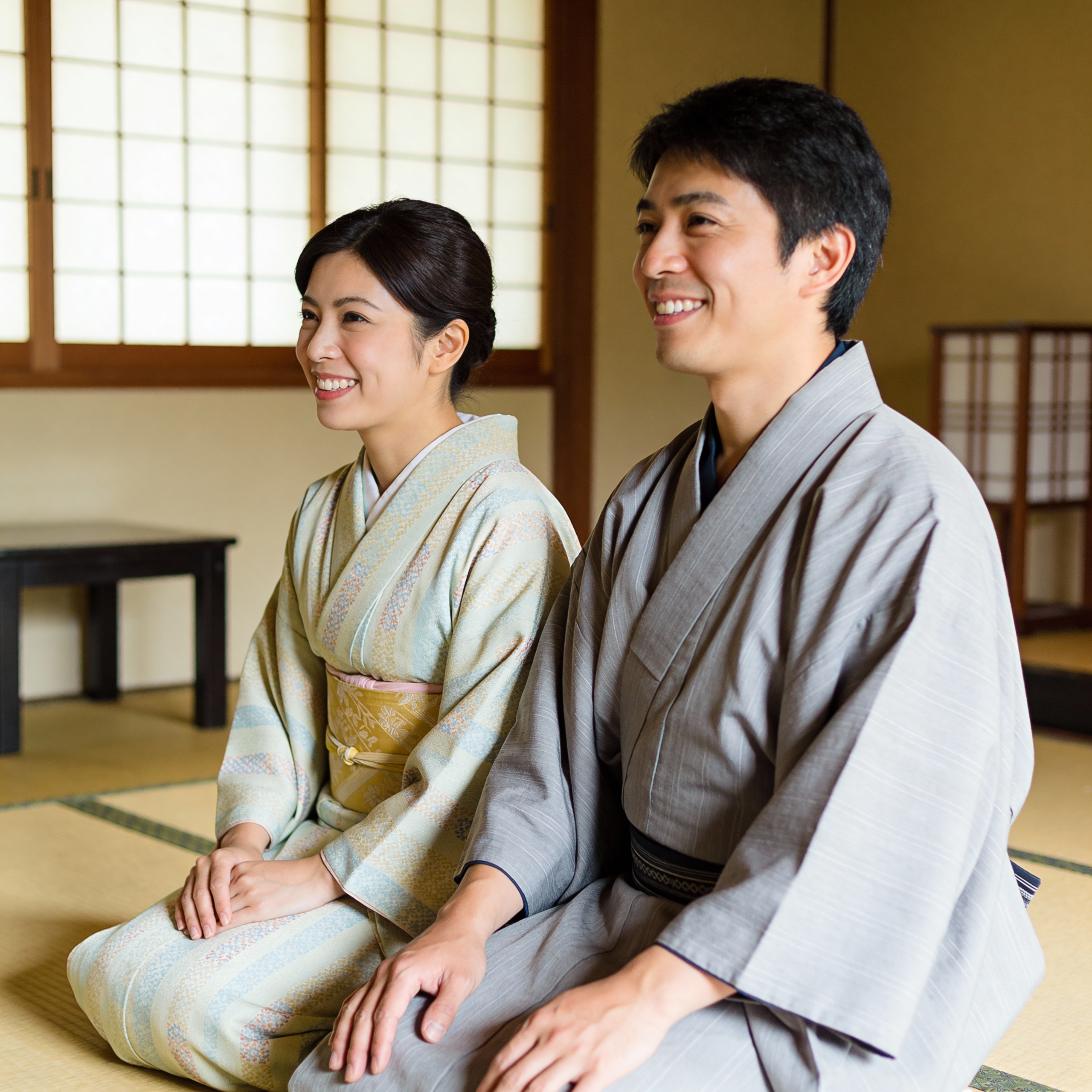 A portrait of a happy couple wearing traditional Japanese Yukata robes in a Ryokan. They are smiling and relaxed. The focus is on the correct way to wear the robe: the left collar is crossed over the right collar (left side on top). Traditional Japanese room background.